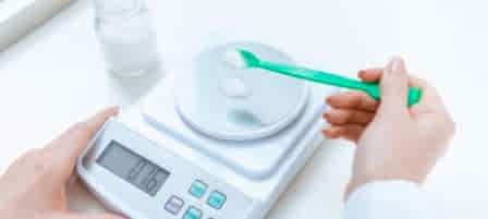 Close-up partial view of chemist weighing reagent on laboratory scales